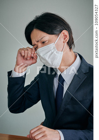 A young male office worker has itchy eyes and rubs them with his fingers A young male office worker has itchy eyes and rubs them with his fingers 109054327