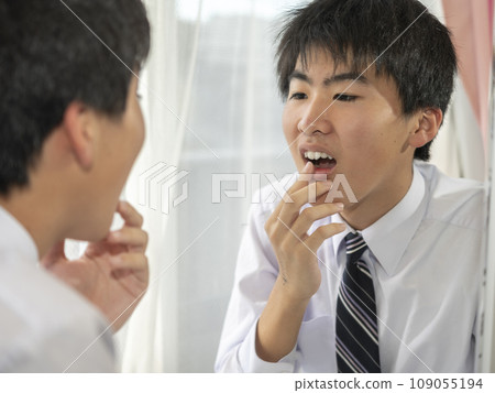A junior high school boy worries about the alignment of his teeth in the mirror at home. A junior high school boy worries about the alignment of his teeth in the mirror at home. 109055194