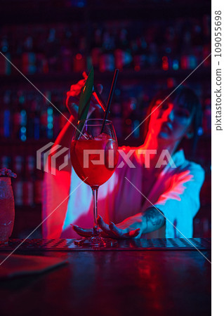 Young beautiful woman, bartender in modern bar, making delicious Aperol Spritz cocktail in neon, decorating with leaf 109055698