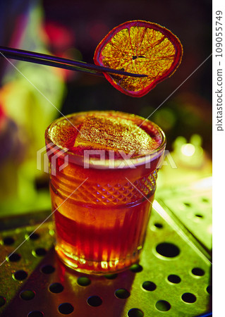 Glass with delicious cocktail, decorated with dry slice of orange. Neon colored bar. Bartender profession 109055749