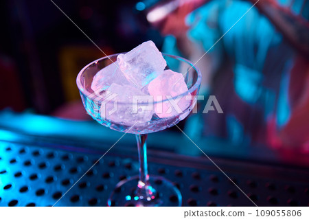 Focus on cocktail glass with ice cubes. Neon light. Modern bar. Preparing sweet and sour cocktails 109055806