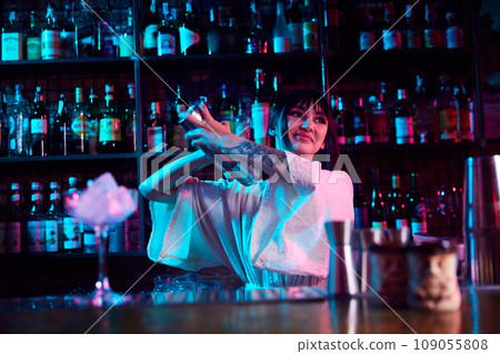 Young beautiful girl, bartender working in bar, nightclub, restaurant, making cocktails, mixing ingredients in shaker 109055808