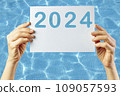 2024, Woman holding cardboard with number 2024 on background of faded lights. Happy New Year 109057593