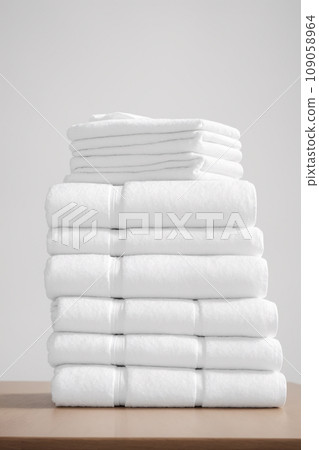 Stack of white towels on a wooden table against a white wall. 109058964