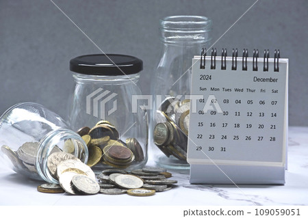 December 2024 calendar and glass jars with multicurrency coins. December 2024 calendar and glass jars with multicurrency coins. 109059051