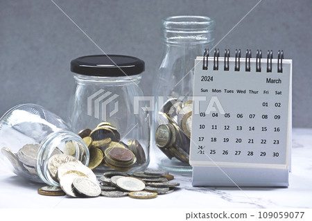 March 2024 calendar and glass jars with multicurrency coins. March 2024 calendar and glass jars with multicurrency coins. 109059077