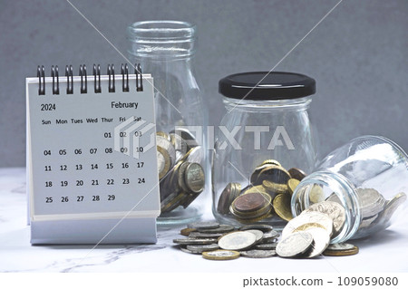 February 2024 calendar and glass jars with multicurrency coins. February 2024 calendar and glass jars with multicurrency coins. 109059080
