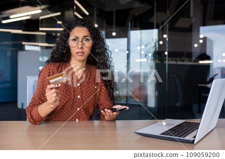 Portrait of disappointed upset woman at workplace, cheated business woman looking at camera holding bank credit debit card in hands, received rejected funds transfer, negative account balance. 109059200