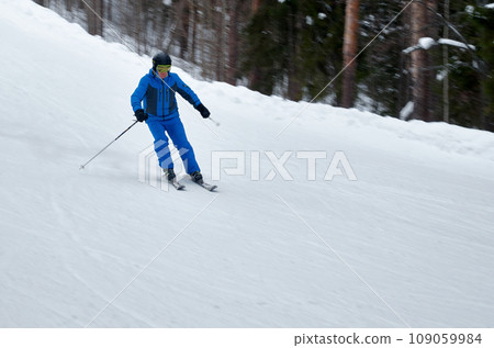 A man in blue sportswear on skis rides down a snowy slope A man in blue sportswear on skis rides down a snowy slope 109059984