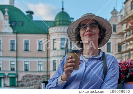 A girl drinks coffee from a paper cup in a coffee shop on the street of an ancient city 109059990