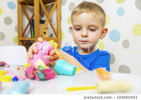 Little boy enthusiastically plays with plasticine, play dough on white table 109060881