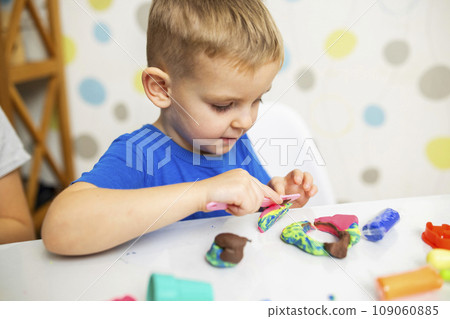 Little boy enthusiastically plays with plasticine, play dough on white table 109060885