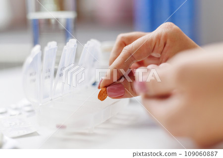 Woman hand putting pills into open pill organizer or plastic pillbox 109060887