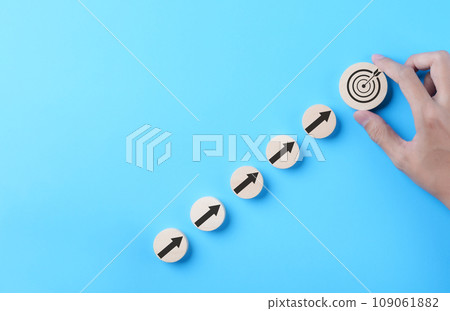 Business achievement goal and objective target concept. Businessman hand putting virtual business target and arrow which screen on round wooden block. Growth investing, Blue background, Copy space, 109061882