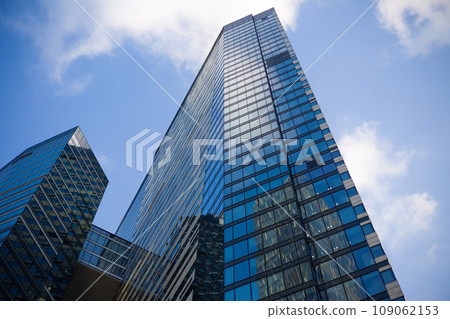 Facade of a narrow glass skyscraper with offices. Multi-storey building made of blue glass with a gentle sky in the background 109062153