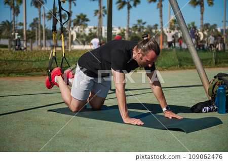 Caucasian middle aged athletic man in black t-shirt exercising with suspension fitness straps in urban background 109062476
