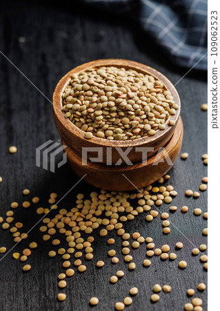 Uncooked lentil legumes in bowl on black table. 109062523