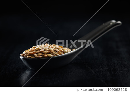 Uncooked lentil legumes in ceramic spoon on black table. 109062528