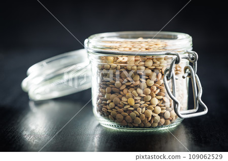 Uncooked lentil legumes in jar on black table. 109062529