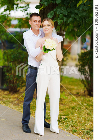 Happy couple newlyweds in the park. The bride wears trousers and a veil. Happy couple newlyweds in the park. The bride wears trousers and a veil. 109062891