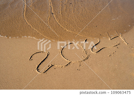 New Year concept. Text 2024 handwritten in sand surface. Blue ocean wave washing away numbers at the beach. Welcoming year 2024 Happy New Year coming new resolutions 109063475