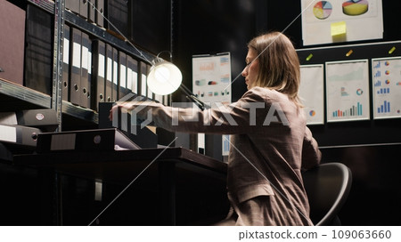 Caucasian criminologist prepares to leave office, packing files and evidence. Female private investigator closing the laptop on workstation after completing research on criminal case investigation. 109063660