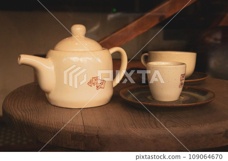 Brown kitchen mock up design. Tableware set. Ceramic beige teapot and two cups stand on a wooden round table in cafe, restaurant Dark key food and drink photo. Morning breakfast. Traditional tea party Brown kitchen mock up design. Tableware set. Ceramic beige teapot and two cups stand on a wooden round table in cafe, restaurant Dark key food and drink photo. Morning breakfast. Traditional tea party 109064670