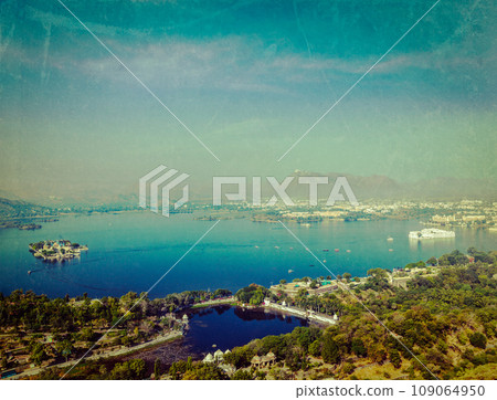 Vintage retro hipster style travel image of aerial view of Lake Pichola with Lake Palace (Jag Niwas) and Jag Mandir (Lake Garden Palace) with grunge texture overlaid. Udaipur, Rajasthan, India Vintage retro hipster style travel image of aerial view of Lake Pichola with Lake Palace (Jag Niwas) and Jag Mandir (Lake Garden Palace) with grunge texture overlaid. Udaipur, Rajasthan, India 109064950