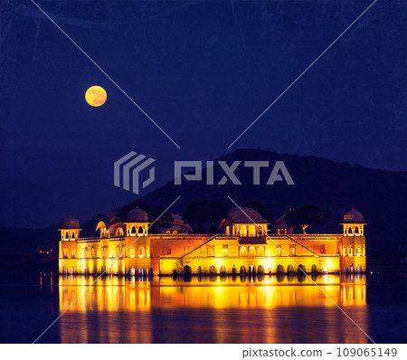 Vintage retro hipster style travel image of Rajasthan landmark - Jal Mahal (Water Palace) on Man Sagar Lake at night in twilight with grunge texture overlaid. Jaipur, Rajasthan, India 109065149