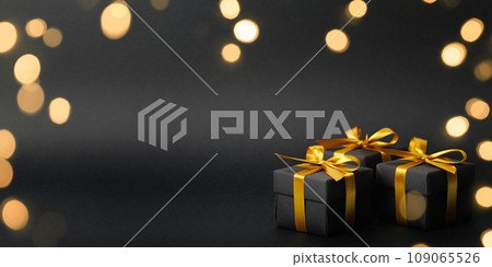 Black gift box with golden ribbon bow on black background 109065526