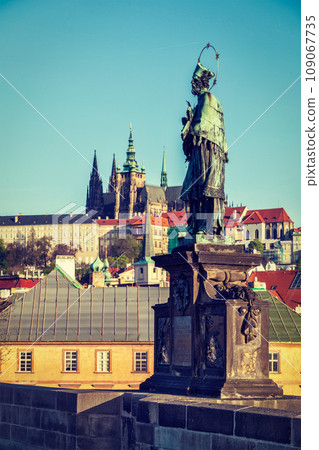 John of Nepomuk (or John Nepomucene) national saint of the Czech Republic statue on Charles Brigde at the site where the saint was thrown into Vltava with St. Vitus Cathedral in background in Prague 109067735