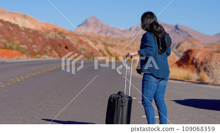 Young woman walking alone through the desert with a suitcase as luggage 109068359