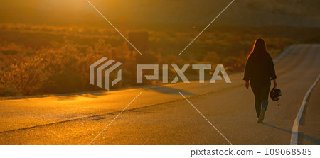 Young Woman walking down a desert road at sunset 109068585