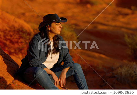 Cowgirl relaxing on a red rock in the desert of Arizona 109068630
