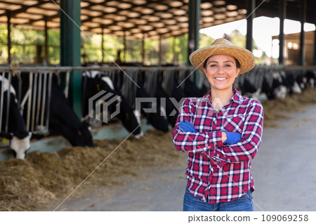 Portrait of female farmer who is standing at her workplace near cows at farm outdoors Portrait of female farmer who is standing at her workplace near cows at farm outdoors 109069258