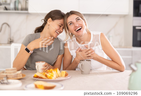 Two women having fun chatting and eating cupcake or pie in home kitchen Two women having fun chatting and eating cupcake or pie in home kitchen 109069296
