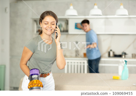 Girl cleans kitchen with vacuum cleaner and has nice conversation on phone with her friend 109069455