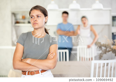 Offended young woman standing at kitchen during argument with husband and mother-in-law Offended young woman standing at kitchen during argument with husband and mother-in-law 109069492