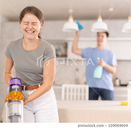 Emotional young girl laughing while vacuuming home kitchen floor Emotional young girl laughing while vacuuming home kitchen floor 109069604