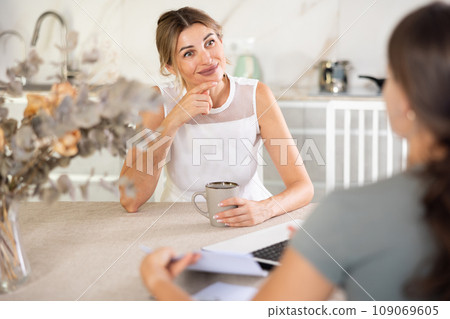 Woman talks to anb agent while sitting at table in kitchen Woman talks to anb agent while sitting at table in kitchen 109069605