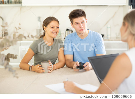 Smiling young couple discussing with female real estate agent at table Smiling young couple discussing with female real estate agent at table 109069606