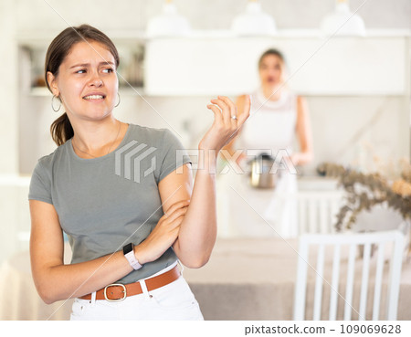 Young girl standing at the table while woman is quarreling with her standing behind 109069628