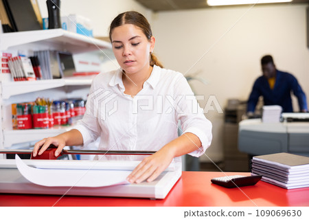 Focused young female typographer trimming the printed work on the cutter in the typography 109069630