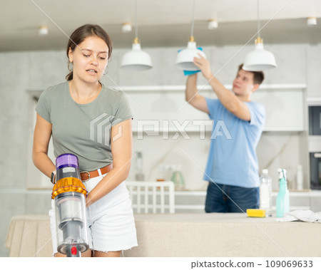 Girl collects dust with vacuum cleaner during group cleaning in kitchen Girl collects dust with vacuum cleaner during group cleaning in kitchen 109069633
