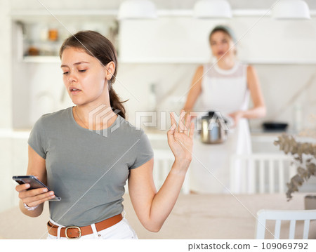 Young girl standing at the table while woman is quarreling with her standing behind 109069792