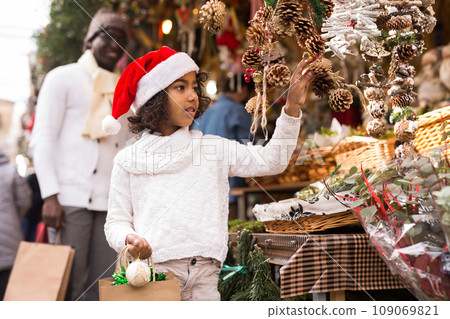 Girl with toy in hand choosing decorations at Christmas market Girl with toy in hand choosing decorations at Christmas market 109069821