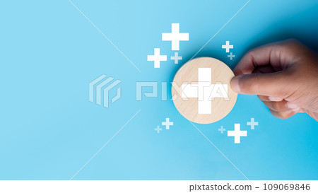 Human hand holding a piece of wood with a plus sign representing positive things such as profits, benefits, development, CSR represented by a plus sign, health insurance. Hand showing a plus sign. 109069846