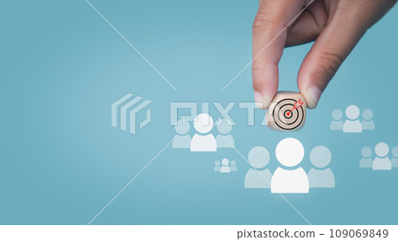 Human hand holds a dart board icon drawn on a wooden block and connects to a target customer on a light blue background It represents the selection of business goals. Marketing plans and strategies. Human hand holds a dart board icon drawn on a wooden block and connects to a target customer on a light blue background It represents the selection of business goals. Marketing plans and strategies. 109069849