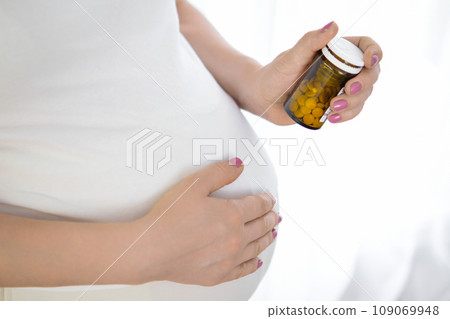 Close up a bottle with pills in pregnant womans hand. Drugs and vitamins during pregnancy. Close up a bottle with pills in pregnant womans hand. Drugs and vitamins during pregnancy. 109069948