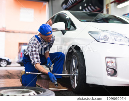 Mechanic engaged in replacement of tyre on car wheel in workshop Mechanic engaged in replacement of tyre on car wheel in workshop 109069954
